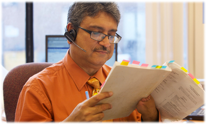 A man consults a document while talking over a headset.